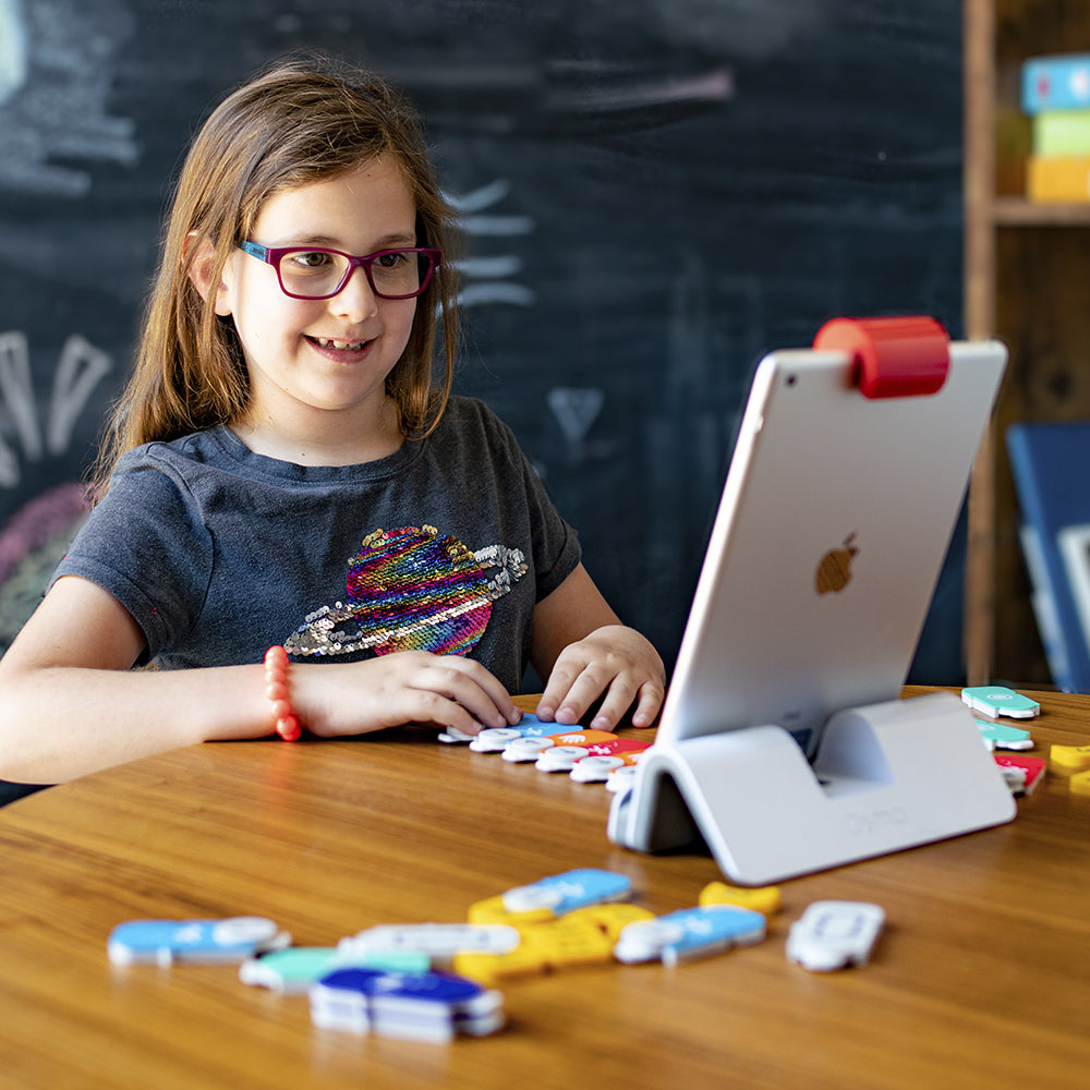 A girl in glasses smiling at the table with Coding blocks spread out in front of the iPad