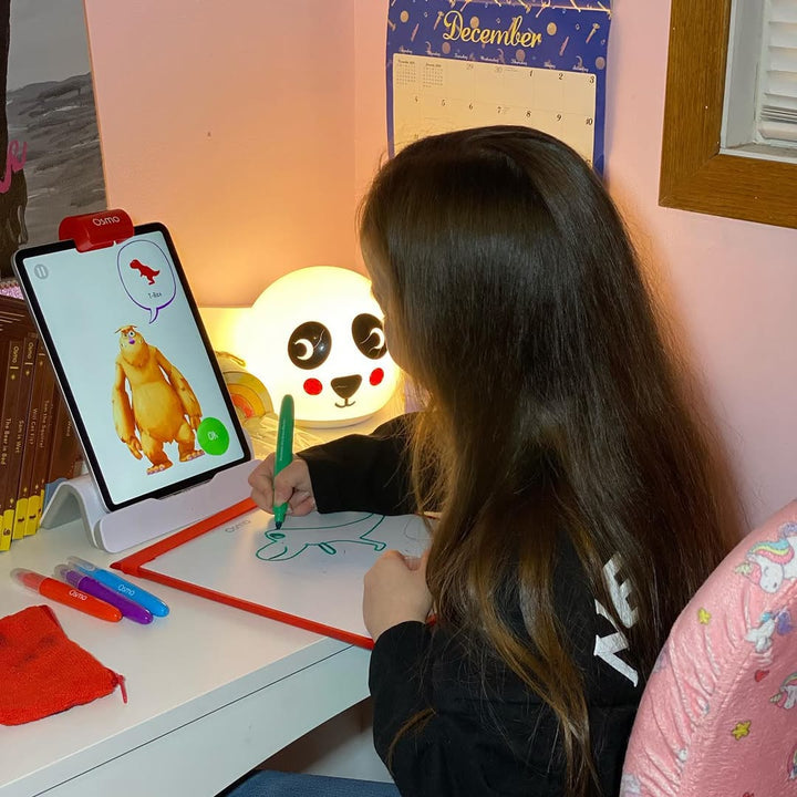 A girl drawing at her desk with the Creative Board and the Monster game on the tablet
