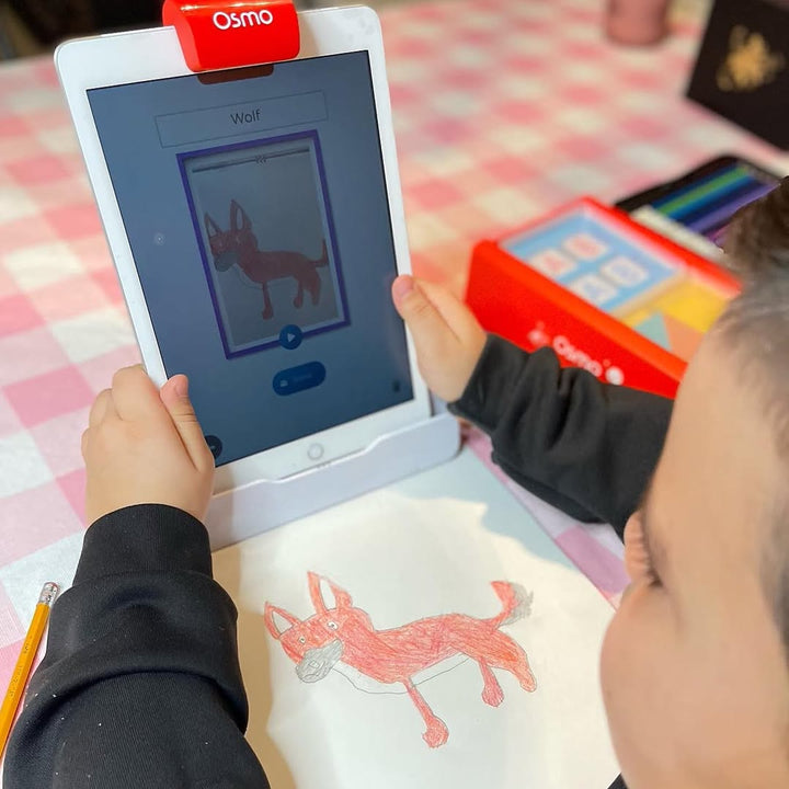 A boy comparing his crayon wolf drawing with the one scanned into Osmo Masterpiece