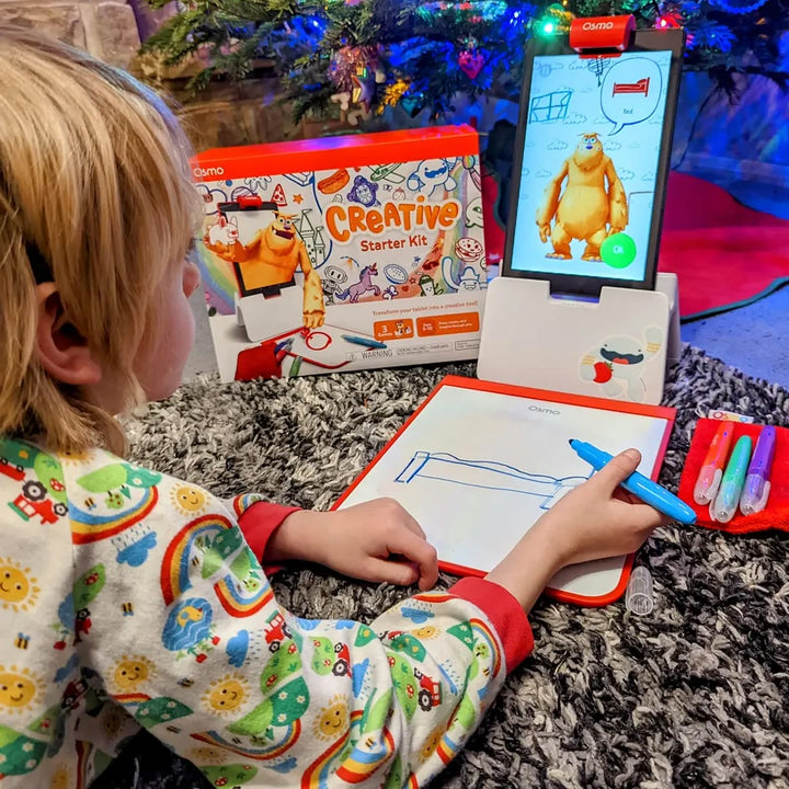 A child in pyjamas drawing on the Creative Board next to the Creative Starter Kit box
