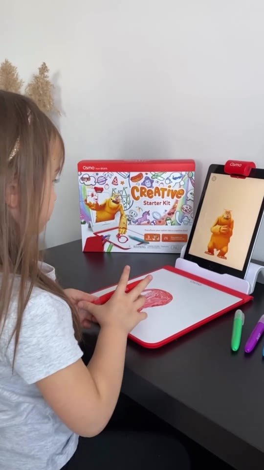 A girl drawing with a blue marker on the Creative Board with the Creative Starter Kit box behind her