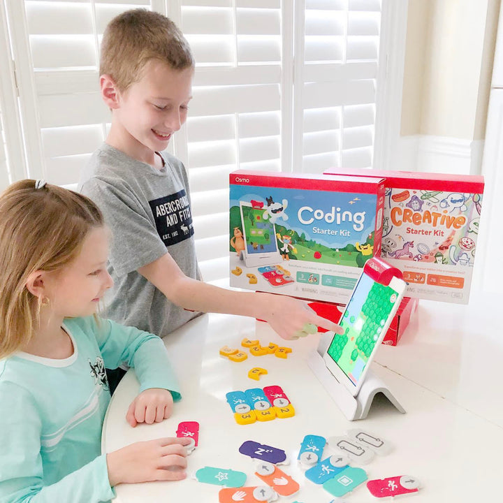 Two kids smiling at a table with Coding blocks, the Coding and Creative Starter Kit boxes and a tablet