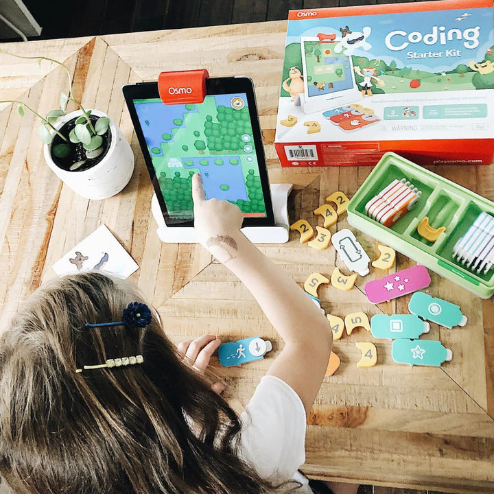 A girl pointing at the tablet next to the Coding Starter Kit box and a tray of coding blocks