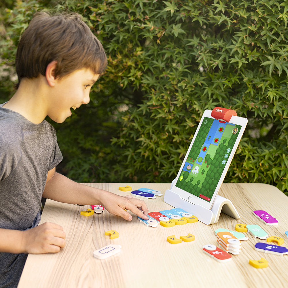 A boy reaching for Coding blocks on a table with the game on the iPad