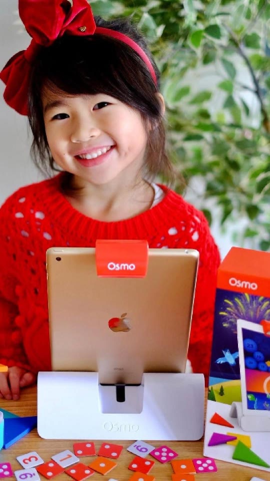 A girl smiling behind her tablet with the Genius Starter Kit and number tiles