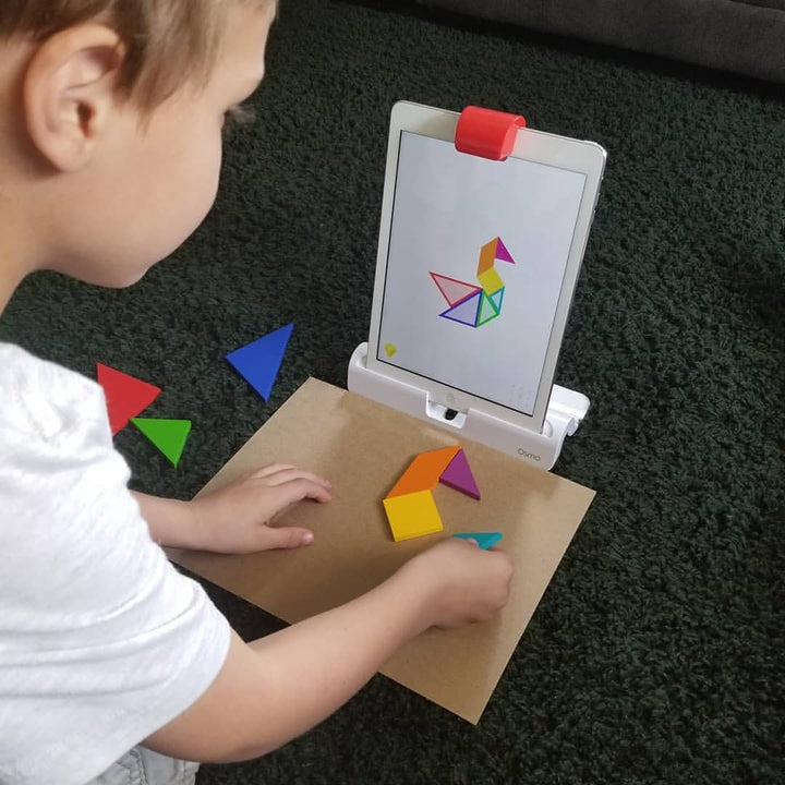A child solving an Osmo Tangram puzzle on the carpet